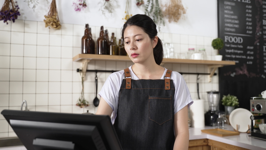Closeup stressed Chinese coffee shop owner is bending over the counter and propping face worrying about business after checking order on the cashier machine. | Shutterstock HD Video #1088504021