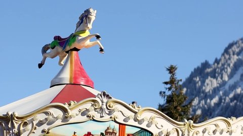 Top horse of a carousel turning with snowed white mountains at the bottom