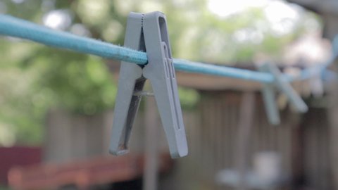 Plastic clothespins hang in a row on the rope. Rope outdoors, on a blurred background in a sunny garden. Clothesline on the street. Clothespins.