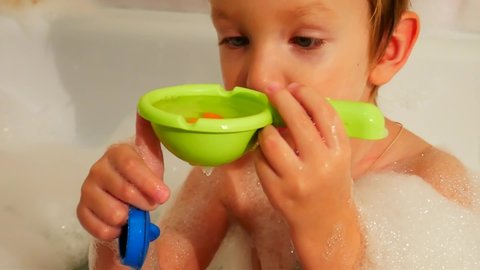 Close-up of a cute little boy sitting in a bubble bath and playing with toys