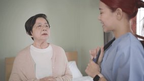 Senior Asian woman talking with Asian woman nurse wearing scrubs in the bedroom. Caregiver visit at home. Home health care and nursing home concept. Slow-motion 4k video.