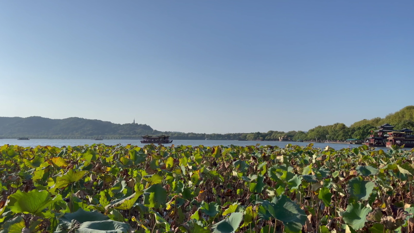 Pan across West Lake scenery in Hangzhou, Zhenjiang China - of lotus leaves, boats on the lake, mountains, to the Jixian Pavilion - a UNESCO World Heritage Site