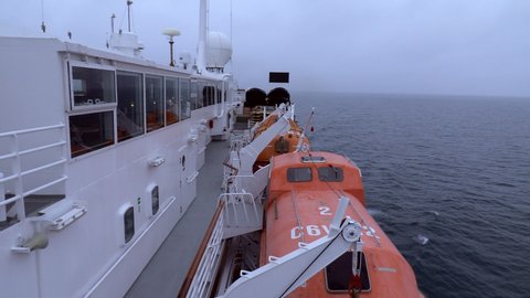 Unique shot of a ship's lifeboats on their davits.   Clip also includes view of upper deck of the ship as well as the open sea.