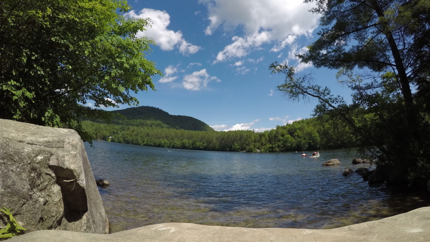 Beautiful Mirror Lake in the state of Maine, panoramic time lapse footage in spring with fast moving clouds against a clear blue sky. Tourist and families kayak and canoe on the crystal clear waters.