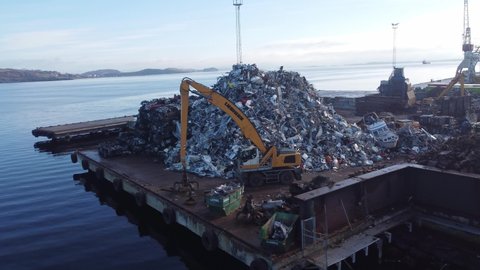 Stavanger , rogaland , Norway - 03 06 2022: Massive pile of old cars and scrap metal on Stena recycling junk yard in Stavanger Norway - Liebherr grabber standing next to pile - Early morning sunrise a