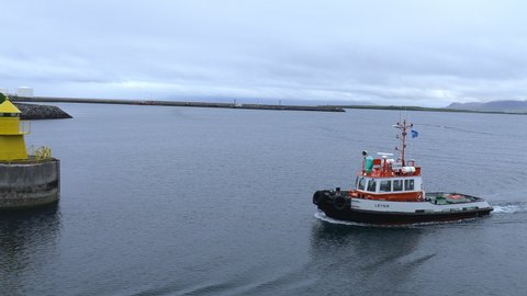 Reykjavik  Iceland - July 2021: A small pilot boat glides past the navigation beacon that guides ships into the harbor at Reykjavik. The boat passes the seawall that protects the harbor from storms. 