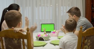 green screen notebook. Parents with two teenage boys talking video call using a laptop, enjoying spending time together on the weekend, at home, at the holiday table prepared for Easter
