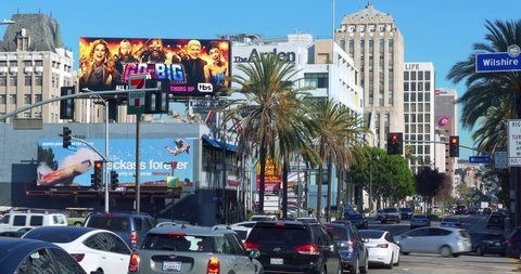 LOS ANGELES, CALIFORNIA - JANUARY 21, 2022: Cars traffic on Wilshire Boulevard at rush hour near giant movie billboard in Los Angeles, California, 4K