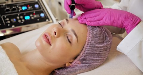 Beautician makes skin care procedure on a  face. Woman in a spa salon on cosmetic procedures for facial care. Cosmetologist making a woman a therapeutic laser processing on a face.
