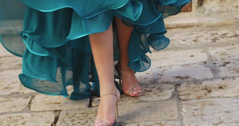 close-up of a dress with many ruffles. a girl in shoes spins around herself in a blue dress that develops by inertia. against the background of the walls of the old city.