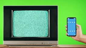 Old television with grey interference screen on green background and smartphone with blue chroma key. Close-up of vintage tv, nostalgia. Gray noise screen and glitches.