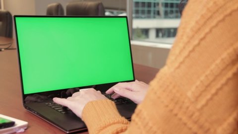 Young woman typing on laptop, takes magnifying glass to examine something on green screen, bring it closer. Chroma key, mockup
