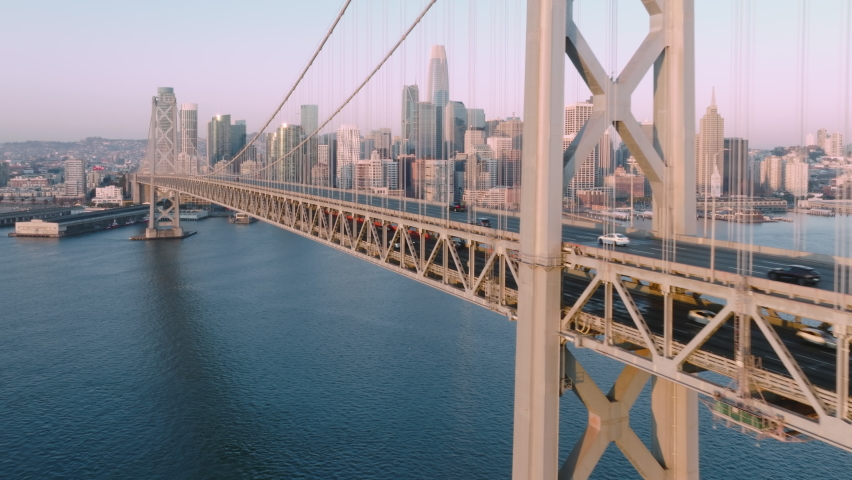 Aerial drone of San Francisco City Skyline and Bay Bridge in gentle golden Sunrise light. 4K drone footage of cars driving by Bay Bridge over calm blue waters to San Francisco downtown, California USA Royalty-Free Stock Footage #1088521493