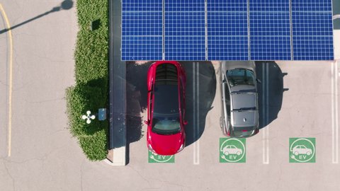 Aerial view of a car parking under solar panels. 4K electric, zero pollution cars on green energy concept on modern city parking lot. Alternative energy for ecological cars under blue solar batteries