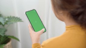 Woman using green screen for copy space closeup. Chroma key mock-up on smartphone in hand, female sitting on bed holding mobile phone and touch screen while looking social.