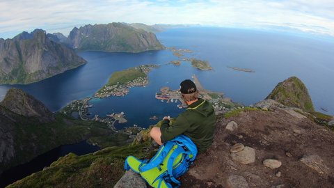 Traveler man sitting on a hill of beautiful norway fjord Reinebringen near Reine town, Lofoten Islands.