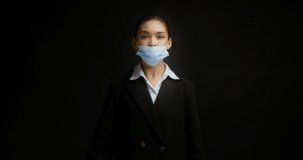 An Asian woman in business clothes shows a video instruction on how to properly wear a medical mask during an pandemic, flu, coronavirus. Thumb down, thumb up, isolated on black background