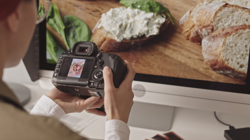 Over-the-shoulder shot of female photographer scrolling food photos on camera while working in studio