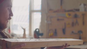 Woodworker blowing dust from wooden plank and examining it while working in carpentry workshop - Powered by Shutterstock - Get 15% off with code: PIKWIZARD15