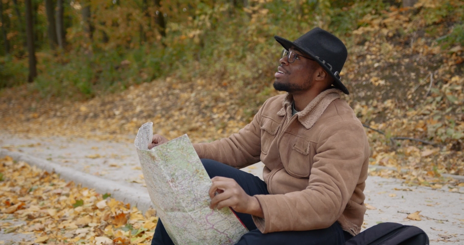 A traveler sits on the roadside with a map
