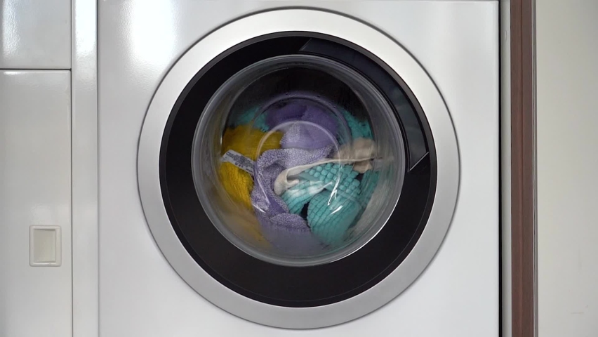 Colorful laundry inside a front loader washing machine spinning counter clockwise Royalty-Free Stock Footage #1088531393