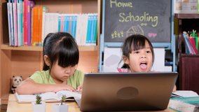 Two Asian female students study online video call Zoom with laptop at home. Two little girls learning at home during quarantine. New Normal. Home schooling.