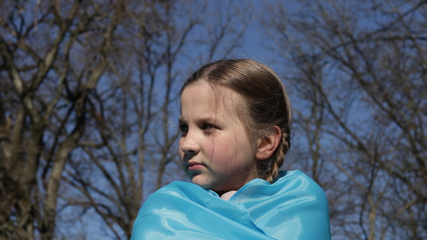 A little girl is covered with the Ukrainian flag with her eyes closed against the sky. Symbol of lack of freedom. War in Ukraine. High quality 4k footage