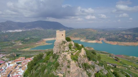 flying around an ancient fortress in medieval Andalusian white village near a blue lake, Iberian landmark and Spanish tourist destination, the village of Zahara de la Sierra. High quality 4k footage