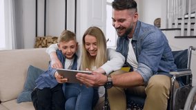 Close up of happy attractive carefree friendly mother,son and dad in wheelchair which celebrating victory in video game using tablet pc at home