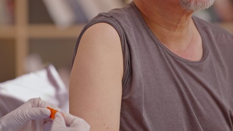 Asian old man got vaccine injection with a syringe needle for an elderly Senior patient. Doctor wearing white gloves and put band aid on his shoulder.