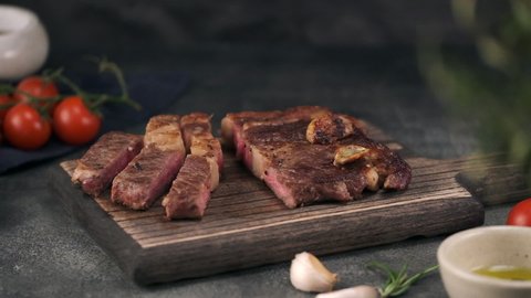Chef with Knife Cuts of Grilled Beef Steak on Rustic Cutting Board on Gray Background. Concept of Delicious Meat Food. Juicy Sliced Rib Eye Steak with Salt. 