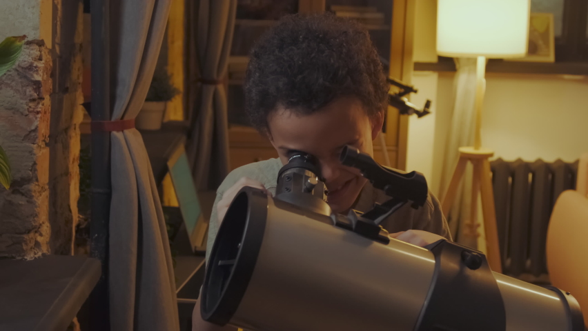 Curious young Black boy having fun watching stars and planets in evening at home using telescope