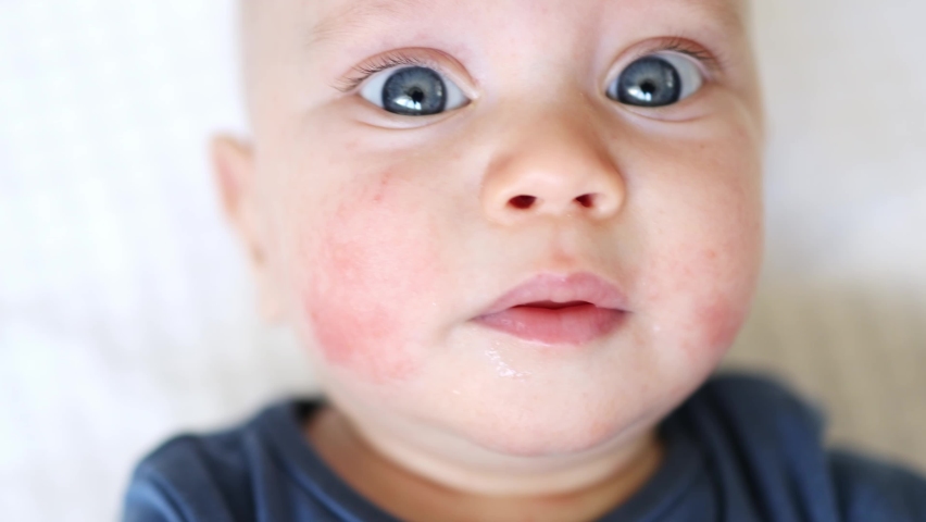 close-up portrait of blue eyed crying baby infant child, kid screaming looking into camera. caucasian baby boy in blue clothes cries opening toothless mouth, showing emotions of sadness or problems.