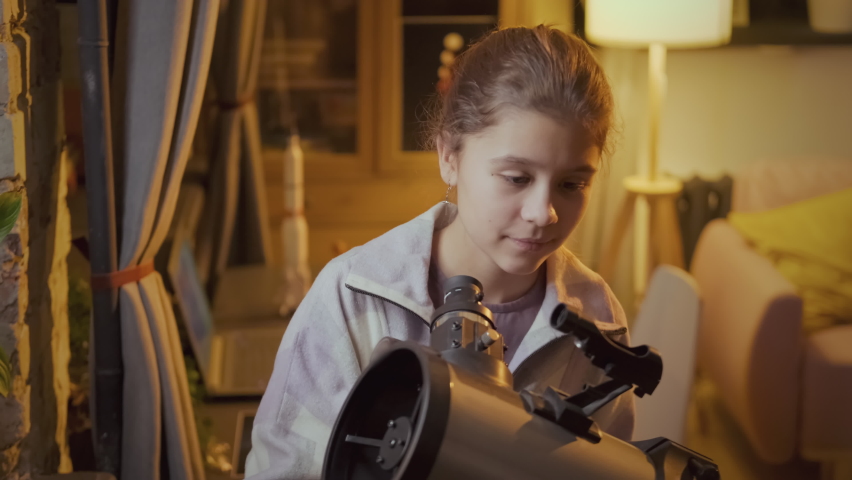 Medium close-up of modern Caucasian girl interested in astronomy looking at stars and planets using telescope