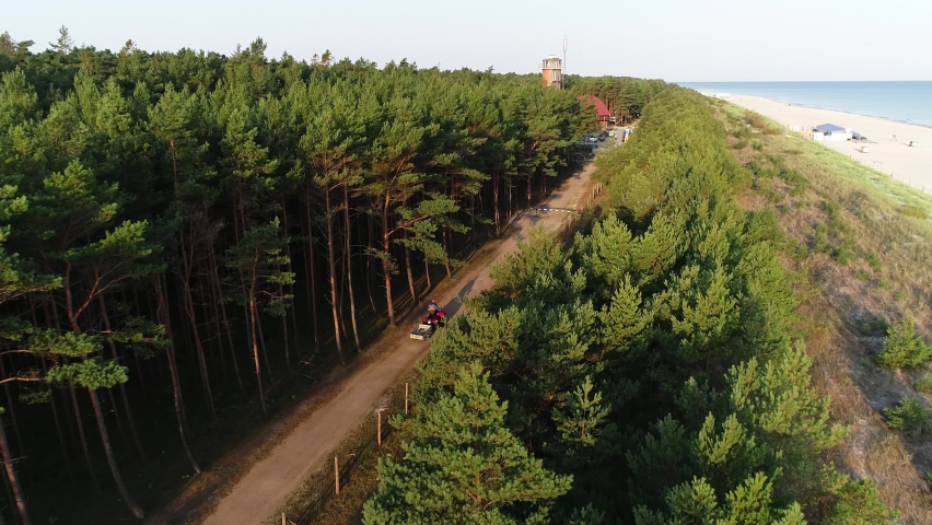 Aerial view of fisherman’s village and atv driving off road at the coastline, to the fishermen’s village. A quad bike driving along a forest road, drone view.