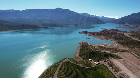 Aerial 4K drone shot over the coast, towards the turquoise water of the Potrerillos Lake, on a sunny day, with perfect blue sky in Mendoza, Argentina. 