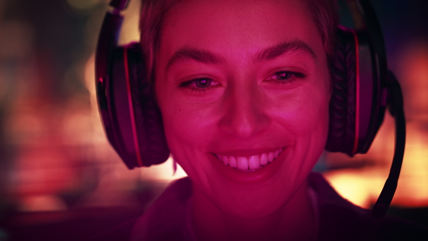 Close Up Portrait of a Stylish Young Female with Short Hair Playing Online Computer Video Game in the Evening at Home. Gamer Discussing Tactics with Teammates while Talking into Headset.