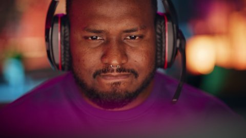 Close Up Portrait of a African American Stylish Young Man with Nose Ring Playing Online Computer Video Game in the Evening at Home. Gamer Discussing Tactics with Teammates while Talking into Headset.
