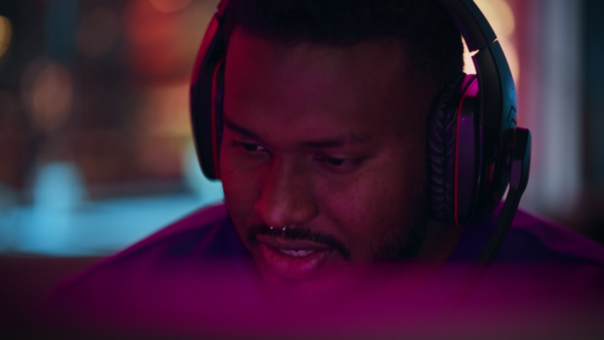 Close Up Portrait of a Black Stylish Young Man with Nose Ring Playing and Winning in Online Computer Video Game in the Evening. Gamer Discussing Tactics with Teammates while Talking into Headset. Royalty-Free Stock Footage #1088539547
