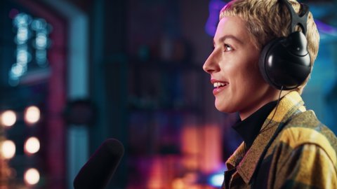 Confident Young Female Talking Into Microphone While Recording Radio Show from Her Loft Apartment. Happy Woman with Short Hair Talking on Camera and Recording Podcast Live on Social Media.