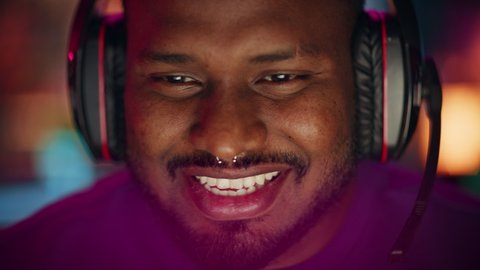 Close Up Portrait of a African American Stylish Young Man with Nose Ring Playing Online Computer Video Game in the Evening at Home. Gamer Discussing Tactics with Teammates while Talking into Headset.
