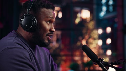 Attractive Young Black Man Talking Into Microphone While Recording Podcast from His Loft Apartment. Happy Multiethnic Male Talking on Camera and Recording Radio Show Live on Social Media.
