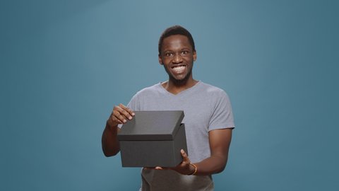 Cheerful man opening present box to see purchase on camera, unpacking cardboard shopping order. Person smiling and unboxing delivery package shipment from ecommerce retail store.