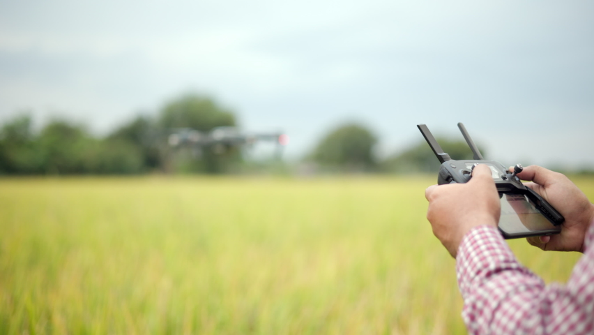 Asian farmer using drone flying navigating above farmland rice field. A young farmer controls a drone in a large scale survey of tenderly touching a young rice in the agricultural plots Royalty-Free Stock Footage #1088541553