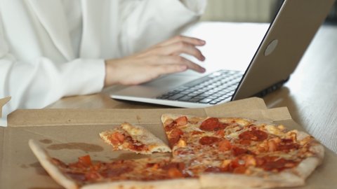 Female hands close-up take slices of pizza. A woman works at a laptop and makes a pizza snack. 