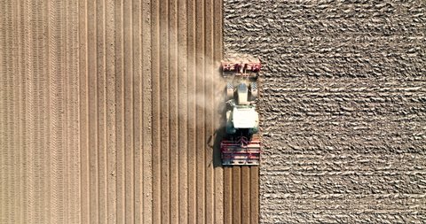Tractor preparing the soil for planting crops during a sunny and dry springtime day. Aerial view drone footage from directly above. 5K video
