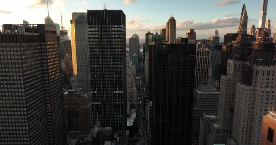 Forwards fly high above street in downtown. Various tall buildings lit by setting sun. Manhattan, New York City, USA