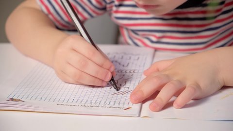 Preschool child learns to write, writes copybook, hands close-up.