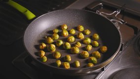 A close up shot of marinated brussels sprouts roasting on a gas hob in a kitchen, as a chef carefully tosses and stirs the vegetables with a wooden spatula to ensure an even cook on a hot frying pan - Powered by Shutterstock - Get 15% off with code: PIKWIZARD15