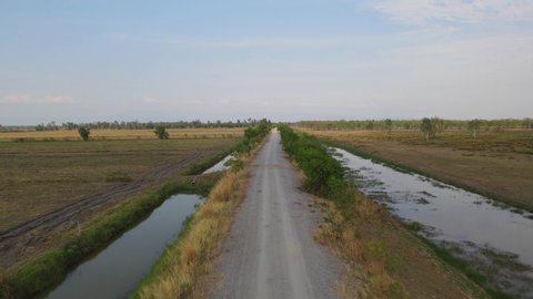 Aerial footage over the dirt road towards the horizon revealing canals on both sides, Pak Pli, Nakhon Nayok, Thailand.